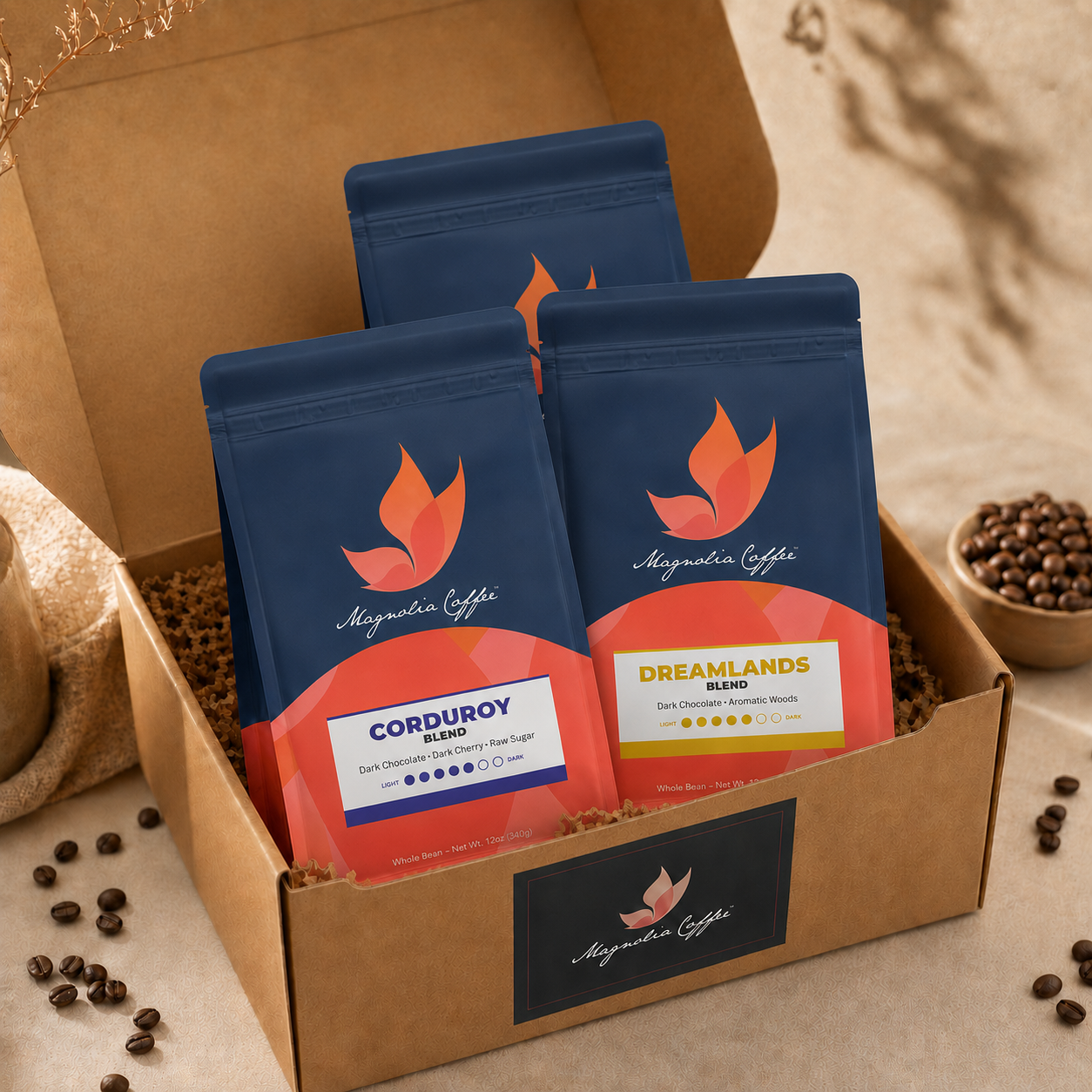 Three coffee packages from Magnolia Coffee in a cardboard box with scattered coffee beans around.